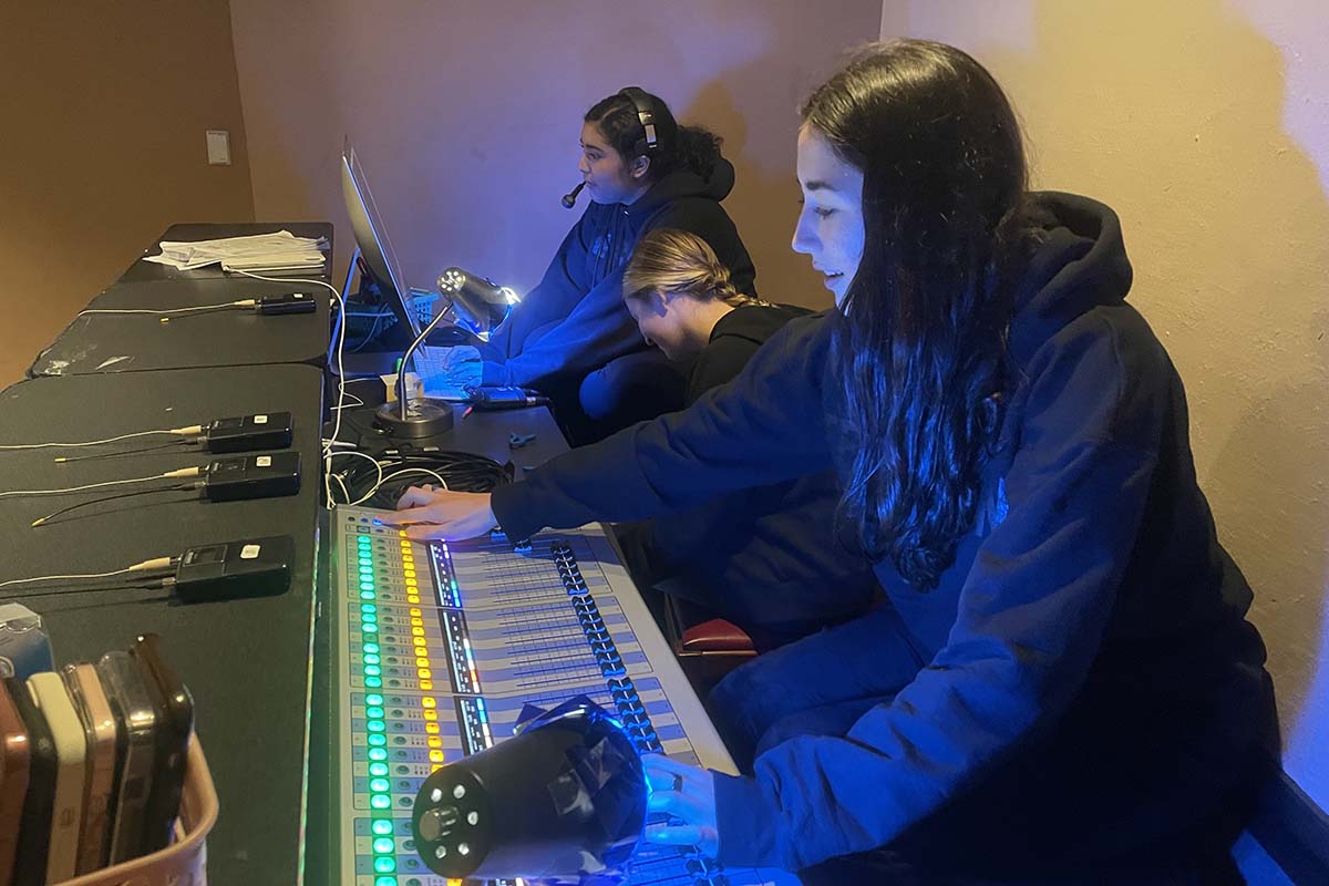 Three theatre tech students are shown at work; one in the foreground operates a sound board.
